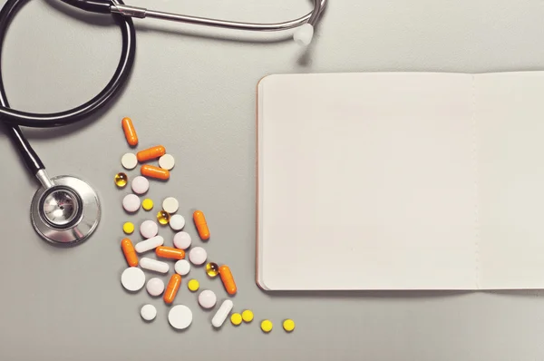 Open notebook with blank pages, pills, capsules and stethoscope