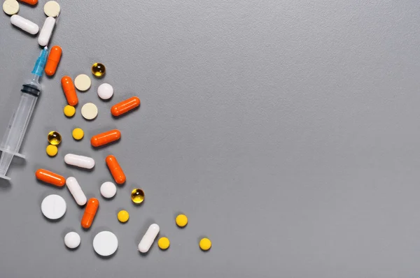 Scattered pills and a syringe on a gray surface