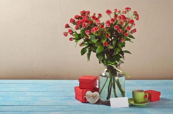 Bouquet of roses, gifts, cup of coffee and card