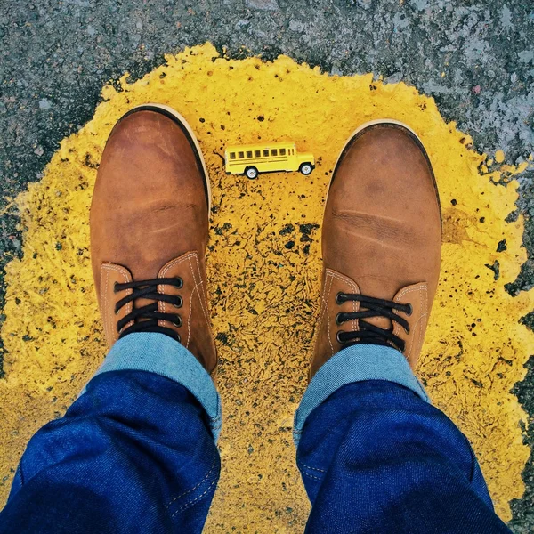 Yellow puddle under man\'s feet with a miniature bus