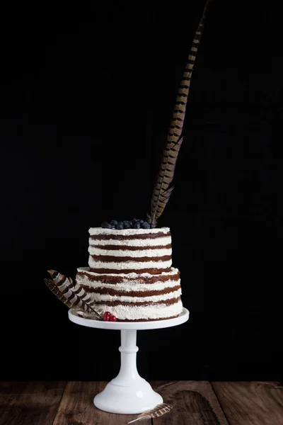 Layered two-storey cake with feathers on a white stand on a black background