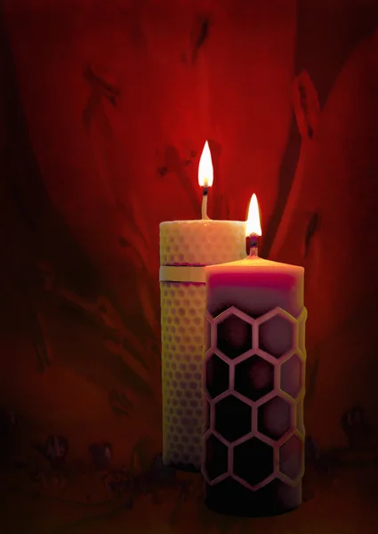 Two beeswax candles flame on a red background