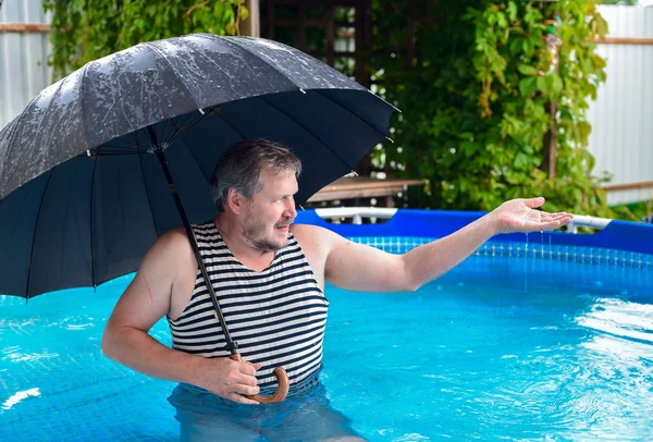 Man in the pool during a rain under an umbrella