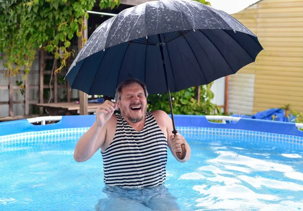 Man in the pool during a rain under an umbrella