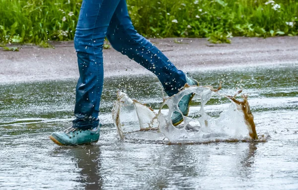 Woman in gumshoes jumping in a puddle. Close up shot of foots in a shoes with water splashes