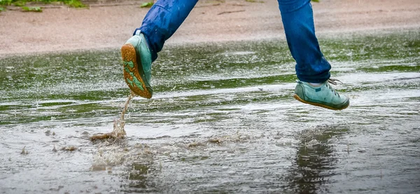 Woman in gumshoes jumping in a puddle. Close up shot of foots in a shoes with water splashes