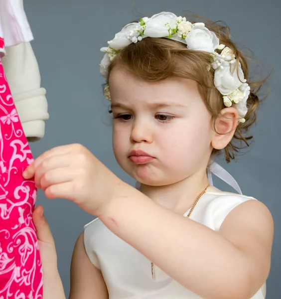 Little beautiful girl in a white dress in the wardrobe with clothes