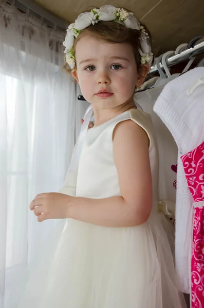 Little beautiful girl in a white dress in the wardrobe with clothes