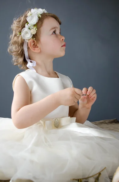 Beautiful little girl in white dress playing with jewelry