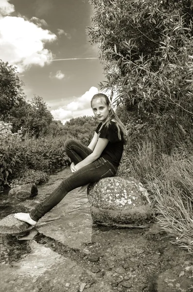 Sad beautiful girl sitting on a rock by the river, black and white