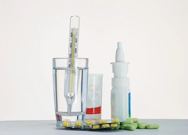 Thermometer in a glass of water and medication for the table