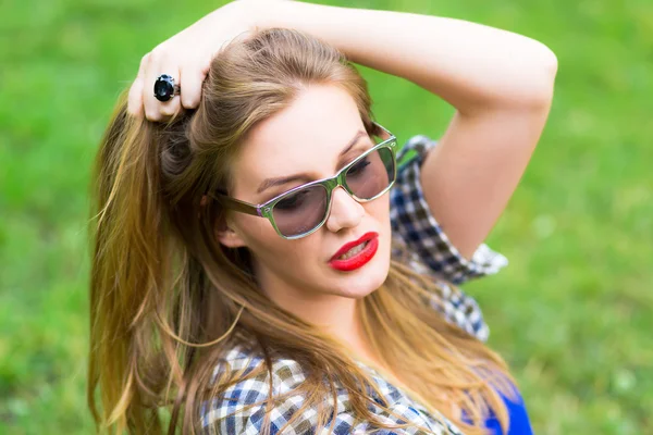 Close up summer fashion portrait of beautiful young sexy woman posing in city park, wearing hipster sunglasses, have natural amazing long blond hair, red attractive lips and perfect skin.