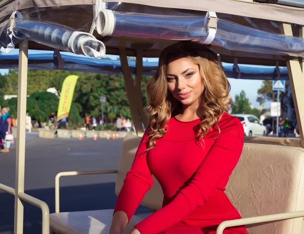 Beautiful tourist girl sitting in white fun trackless train for sightseeing,travel, tourism, summer vacation, sightseeing and people concept.Pretty woman on vacation in Europe in red dress