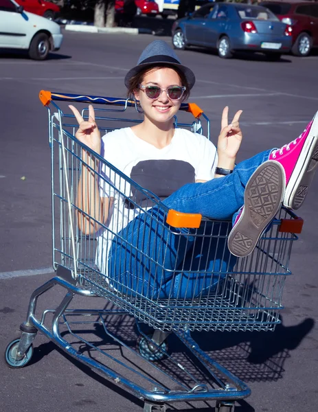 A young woman sitting in a large shopping cart and shouting for joy with her hands up in the air.Girl sitting in shopping cart