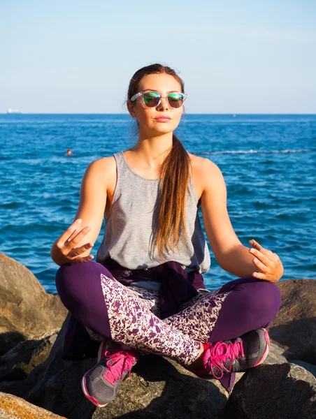 Young beautiful woman meditation on beach.Young girl doing yoga at sea.woman meditating in lotus yoga on coast of sit at the seaside on the rock and meditating in yoga pose