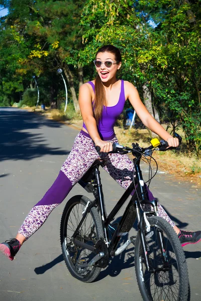 Young Woman biking in city park on bicycle. Happy girl on bike cycling outdoors in summer smiling of joy during outdoor activity.