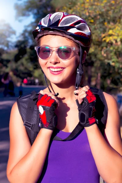 Young woman on the bicycle wearing on the helmet.Bike helmet - woman putting biking helmet on outside during bicycle ride.Woman wearing biking helmet. Close-up portrait of female cyclist.Cheerful lady