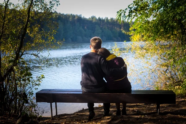 Silhouettes of hugging couple sitting on bench against the lake at sunset