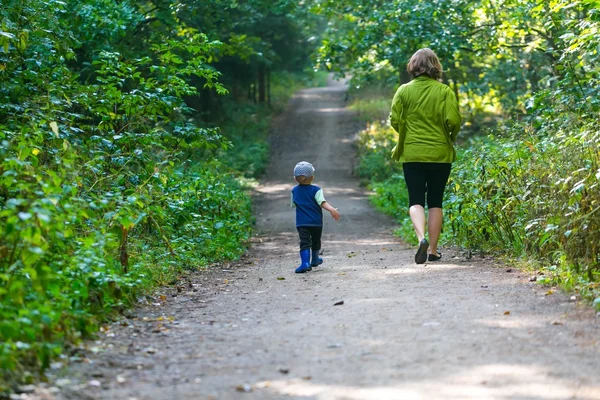 Little boy and mother running and playing in forest at summer.