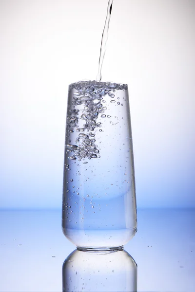 Water pouring into full drinking glass