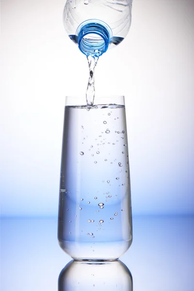 Water pouring from plastic bottle into full drinking glass