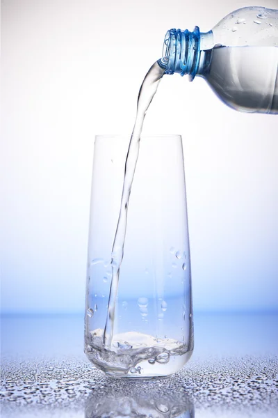 Water pouring from bottle into drinking glass on drops