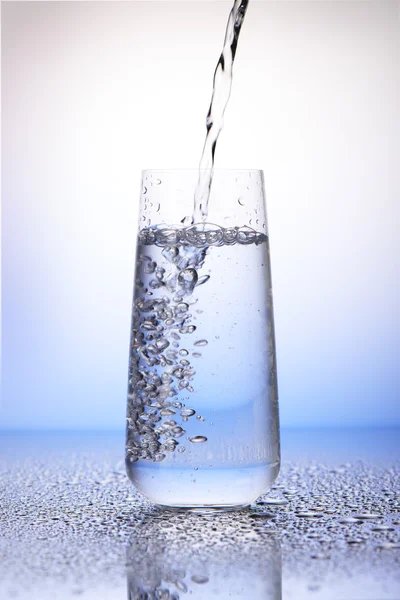 Water pouring into two-third full drinking glass