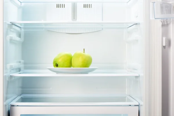 Two green apples on white plate in open empty refrigerator