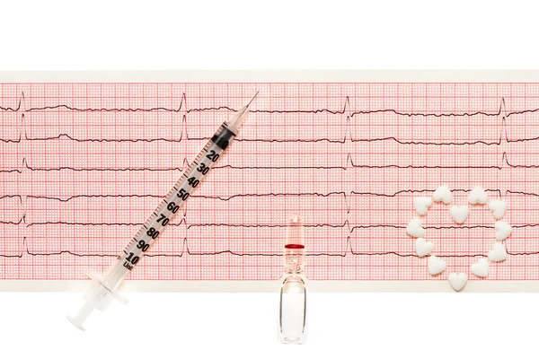 Heart made of white heart shape tablets, transparent white glass ampoule with a drug and plastic syringe with open needle on paper ECG results