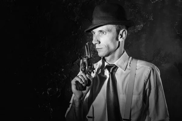 Handsome detective in hat holding a gun in the dark