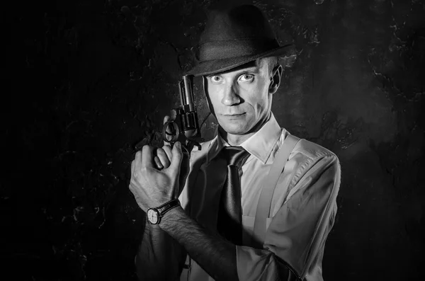 Handsome detective in hat holding a gun in the dark