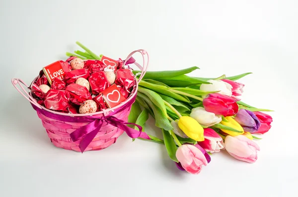 Candies basket and bouquet of tulips isolated on white background