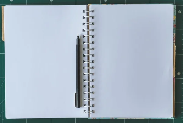 White Notebook blank cover with pen on green cutting mat.