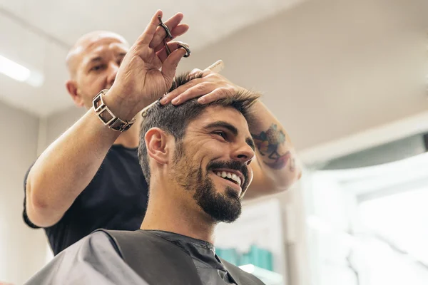 Hairstylist making men\'s haircut to an attractive man.