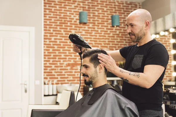Hairstylist making men\'s haircut to an attractive man.