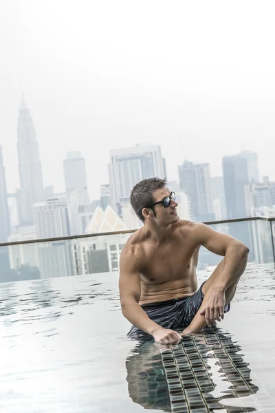 Young attractive man at the swimming pool in roof at skyscraper.