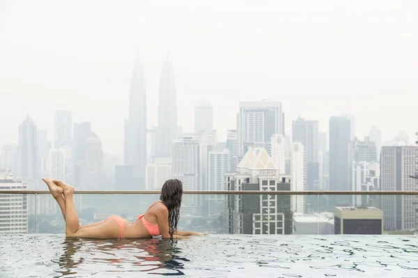 Beautiful woman in swimming pool watching the city
