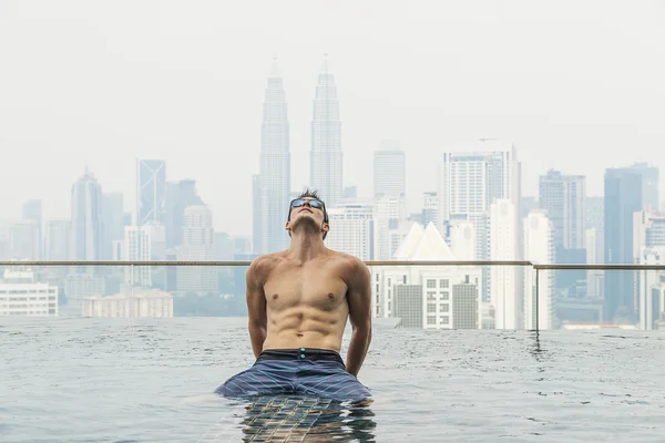 Young attractive man at the swimming pool in roof at skyscraper.