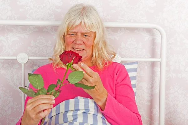 Cheerfull woman in bed with rose