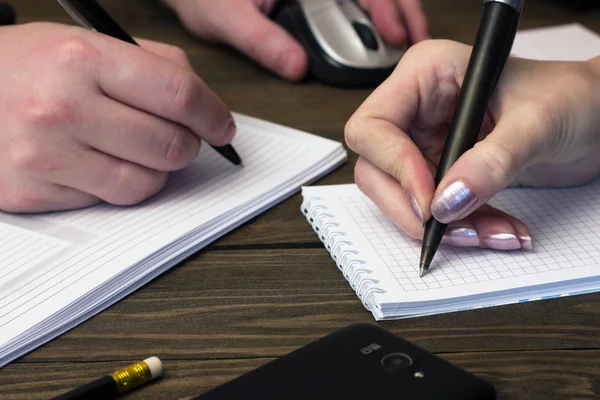 Two hands make notes in a notebook black  pens