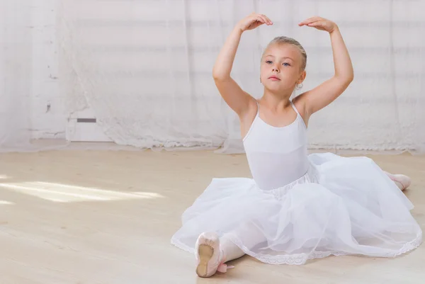 Young ballerina in white clothes sitting on the floor during the training in dance class.