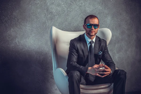 Brutal sexy businessmen in suit with tie and sunglasses sitting on chair. Boss concept.
