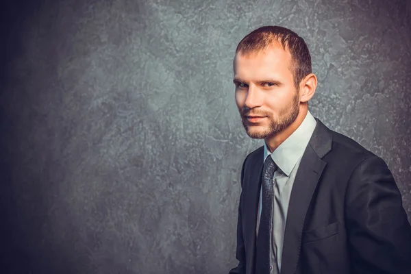 Brutal business man in suit standing near the black wall