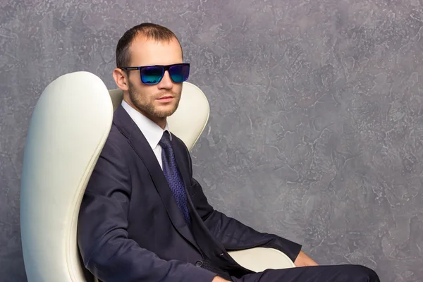 Brutal businessmen in suit with tie and sunglasses sitting on chair. Boss concept.