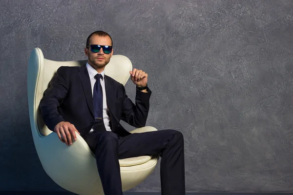 Brutal businessmen in suit with tie and sunglasses sitting on chair. Boss concept.