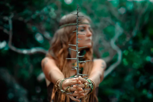 Portrait of beautiful shaman woman holding branch with thorns in