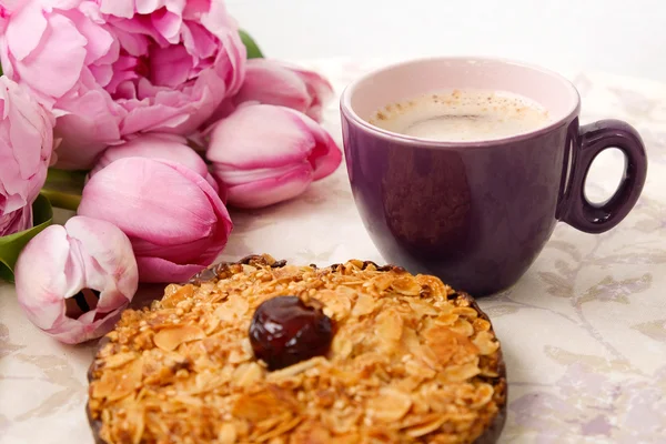 A cup of coffee, a  cookie and rose flowers on the table