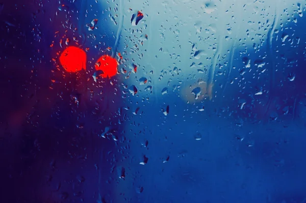 Window of the bus with rain drops on it and the red lights.