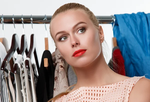 Beautiful blonde woman suffering near wardrobe rack
