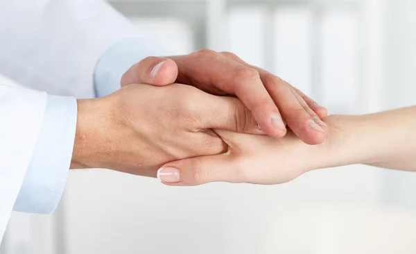 Friendly male doctor hands holding female patient hand